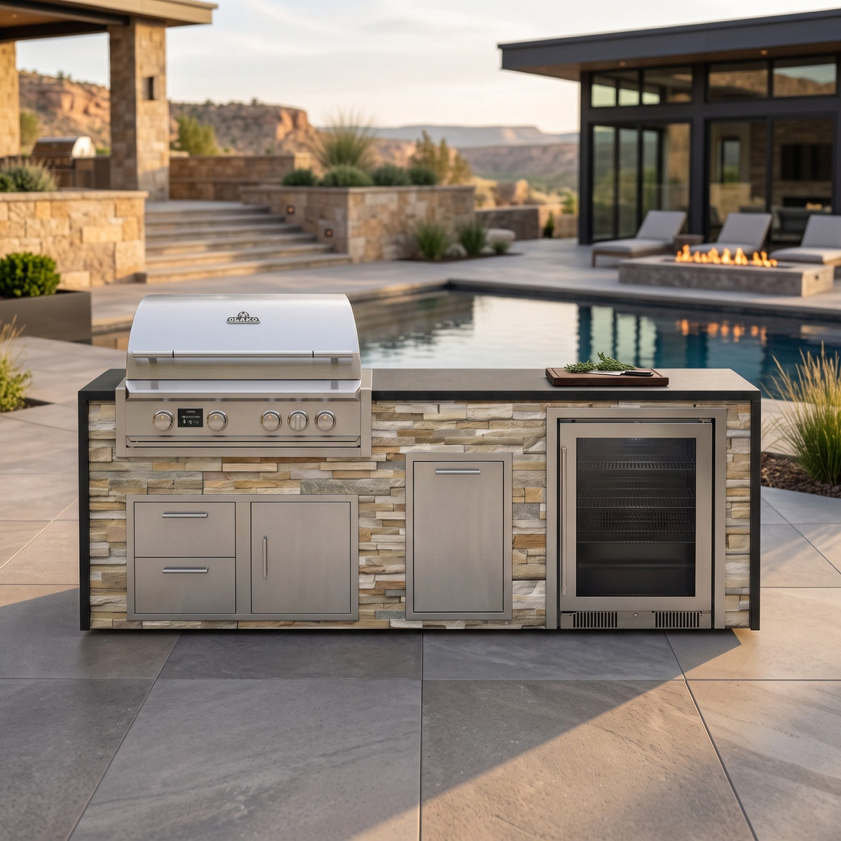 Sunkissed Dune outdoor kitchen with beverage cooler and Charred Onyx granite top on a stone patio facing the pool and fire pit with desert hills in the distance