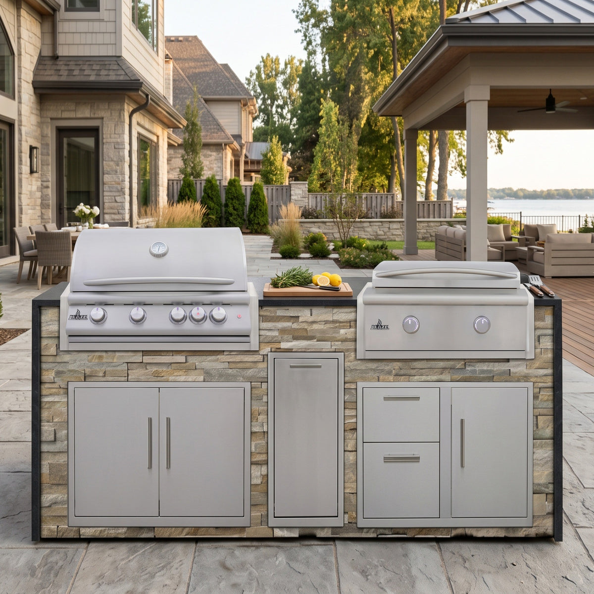 Sunkissed Dune grill and griddle island with Charred Onyx granite top on a stone patio by a covered pergola with a lake view