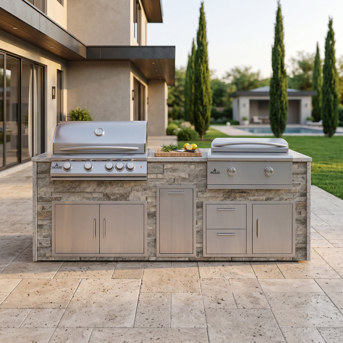 Tuscan Hearth grill and griddle island with Frosted Ember granite top on a travertine patio next to the house with lawn and pool beyond