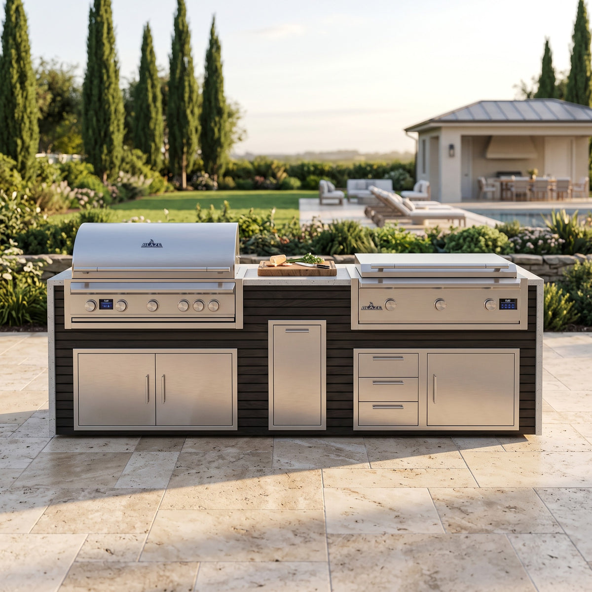 Cindered Ash grill and griddle island with Frosted Ember granite top on a travertine patio facing the lawn, pool and pool house framed by cypress trees