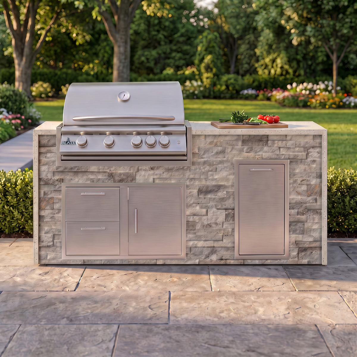 Tuscan Hearth grill island with Frosted Ember granite top and a cutting board of fresh tomatoes on a paver patio facing the lawn
