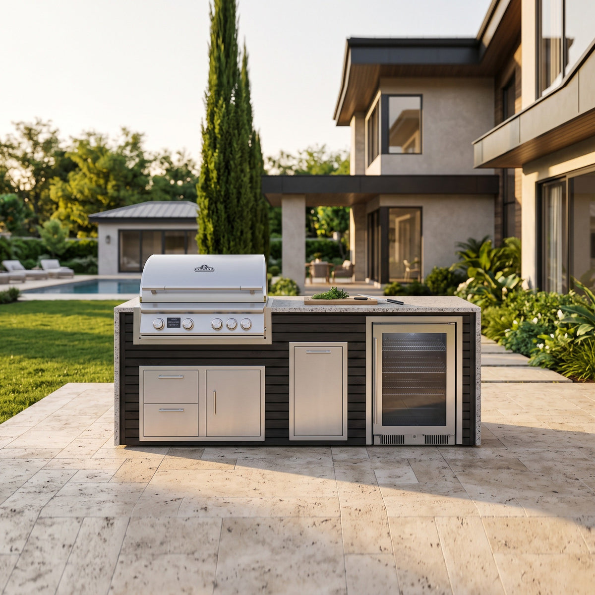 Cindered Ash outdoor kitchen with beverage cooler and Frosted Ember granite top on a travertine patio by a two story home with the pool and pool house across the lawn