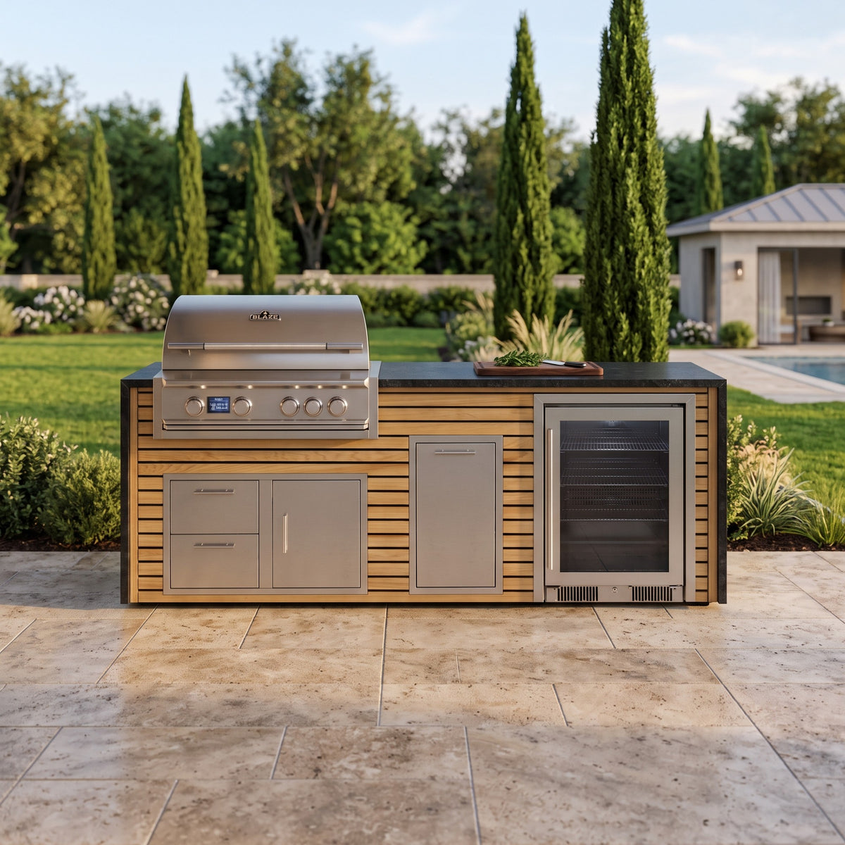Warmed Acacia outdoor kitchen with beverage cooler and Charred Onyx granite top on a travertine patio by the lawn with tall cypress trees and a pool house