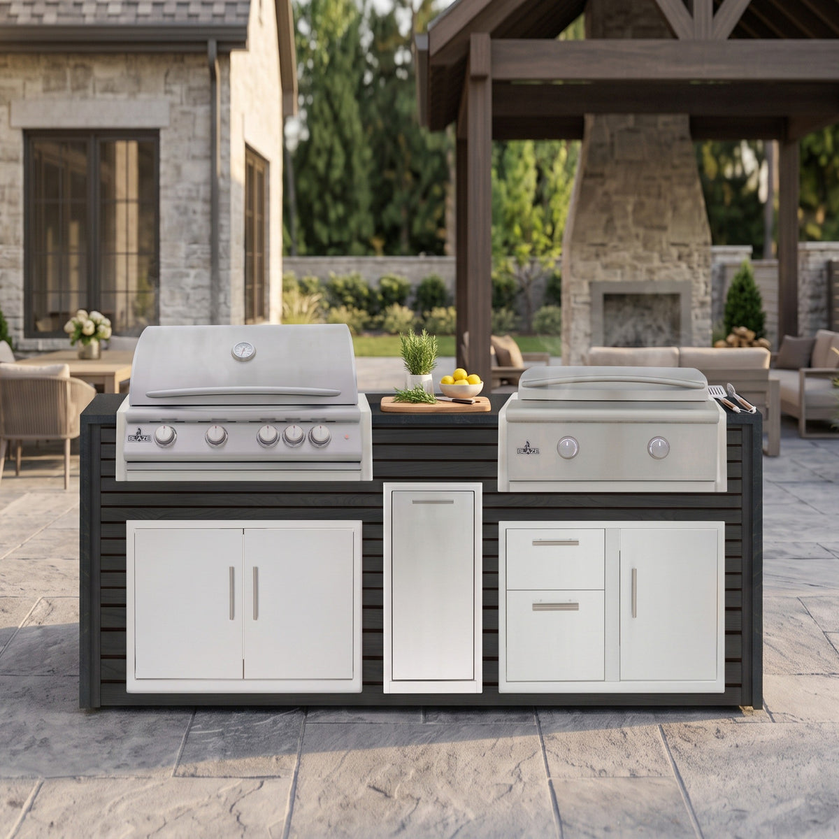 Cindered Ash grill and griddle island with Charred Onyx granite top on a stone patio near an outdoor fireplace pavilion