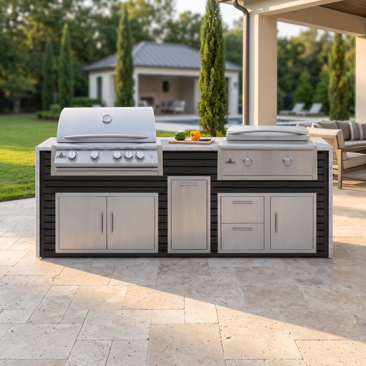Cindered Ash grill and griddle island with Frosted Ember granite top on a travertine patio by a covered porch with a pool house beyond