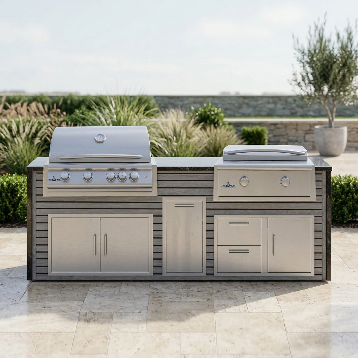 Drifted Cypress grill and griddle island with Charred Onyx granite top on a travertine patio framed by ornamental grasses and a potted olive tree
