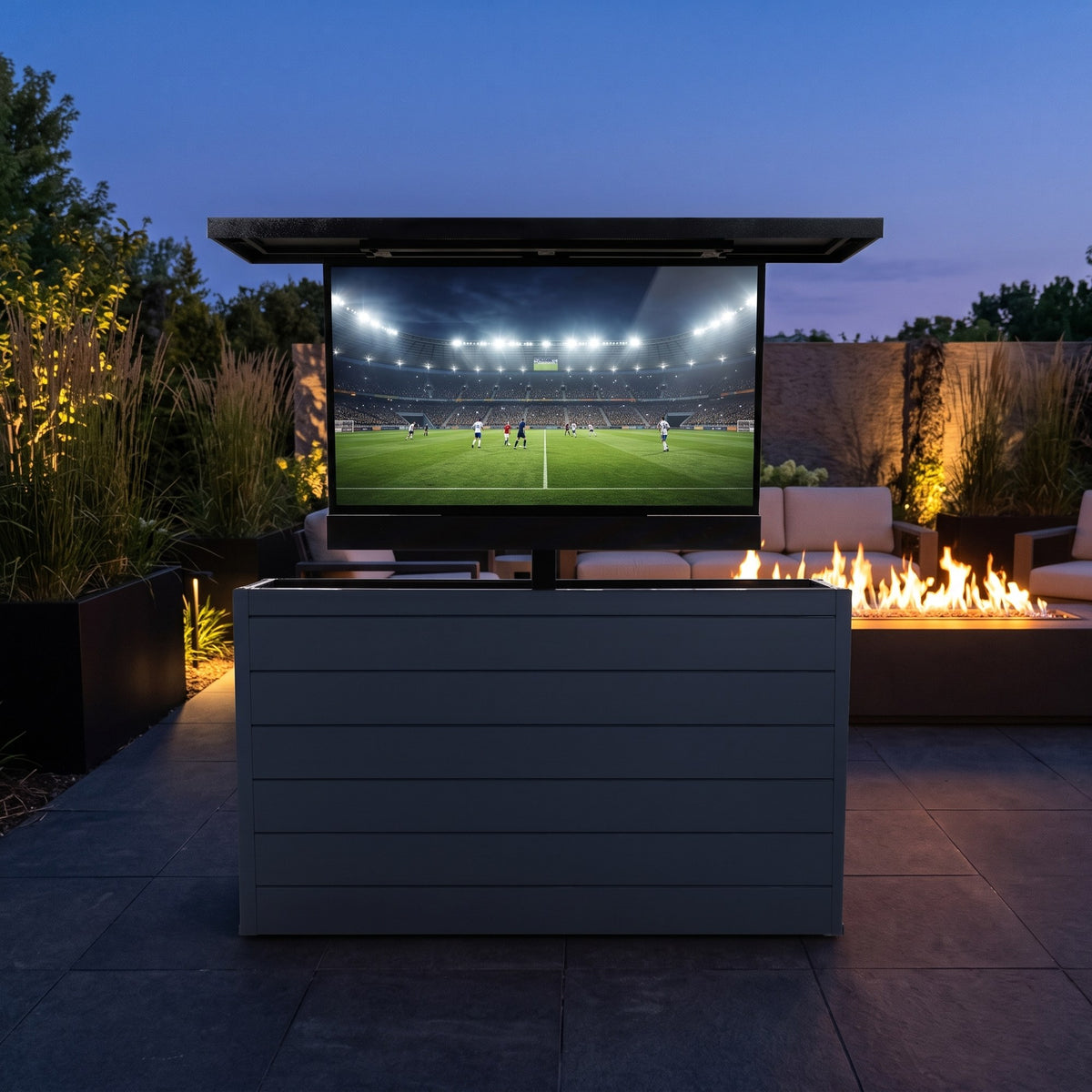 Midnight Graphite 6 inch ArtisanPlank outdoor TV lift cabinet with the TV raised on a dark paver patio at dusk beside a linear fire feature