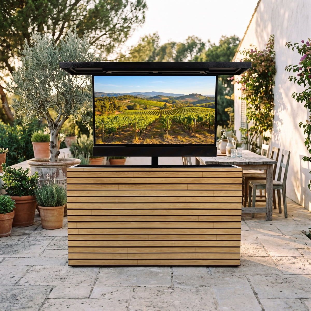 Warmed Acacia 2 inch horizontal ArtisanPlank outdoor TV lift cabinet with the TV raised on a Mediterranean terrace with olive trees