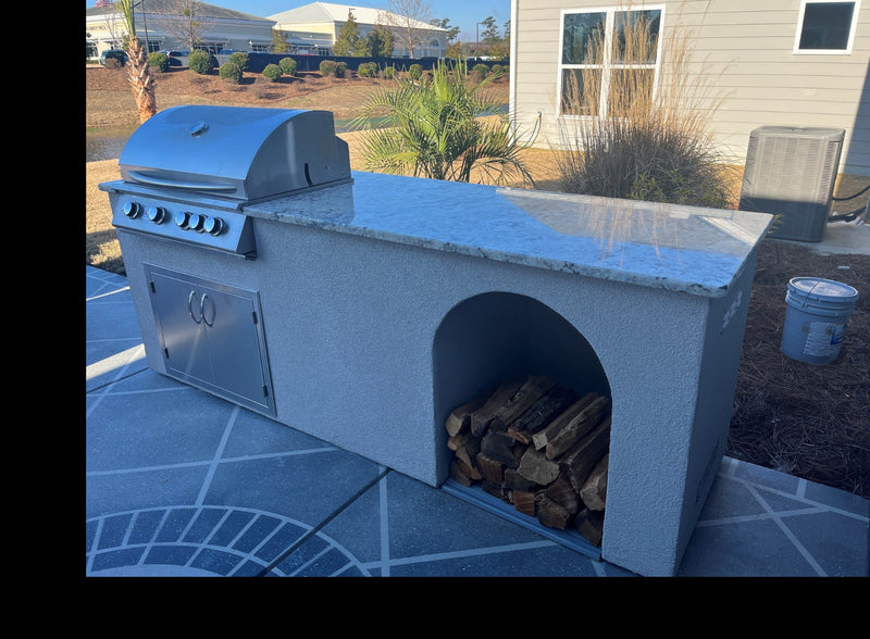 Stucco outdoor kitchen island with built-in grill, granite countertop, and open firewood storage